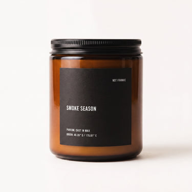 Smoke Season candle by NOT FRANKIE in amber glass jar, a warm smoky fragrance with chestnut, vanilla and wood notes, photographed on a clean white background.